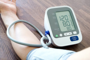 close up of arm on a table or desk, attached to a digital home blood pressure device. Blood pressure shows 120 over 80, showing lower risk of stroke.