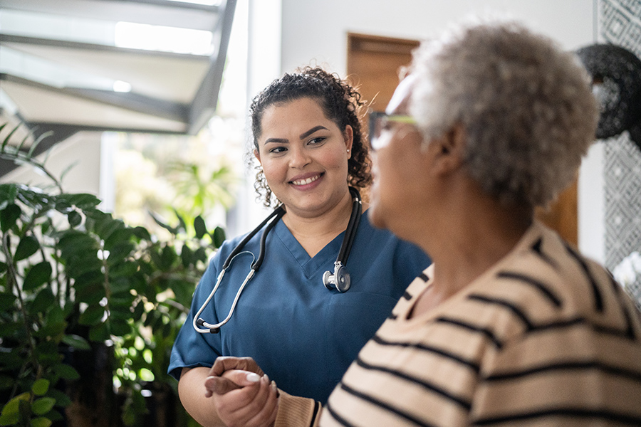 Home healthcare or Home care: what's the difference? Image of caregiver helping patient walk at home. Article explores the difference between home healthcare and home care.