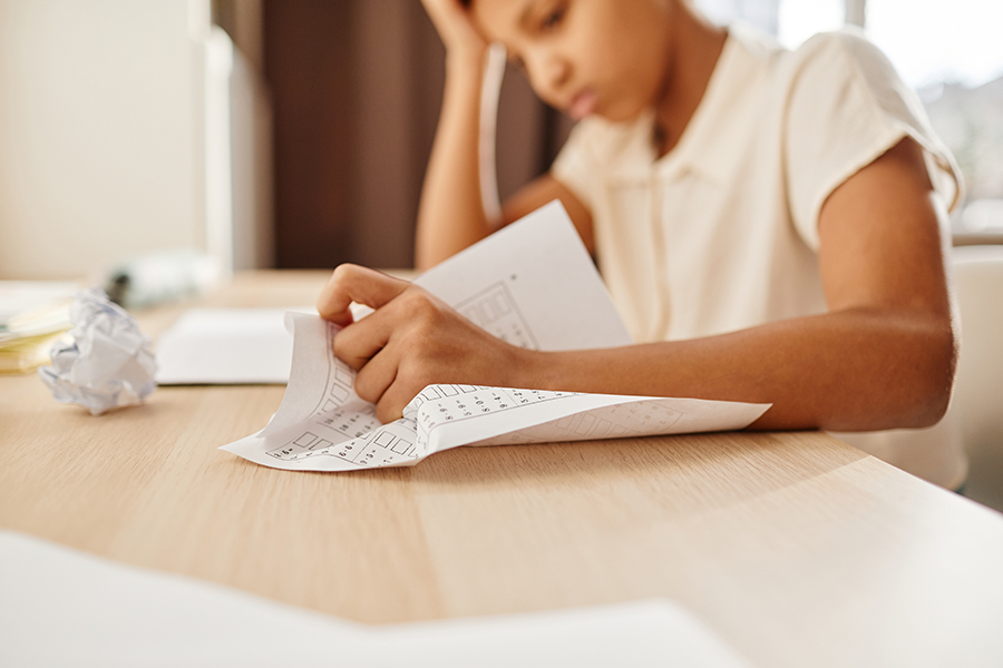 types of IQ testing and other educational testing for children. photo of young girl 8-10 years old, crumpling up homework on her desk, looking anxious.